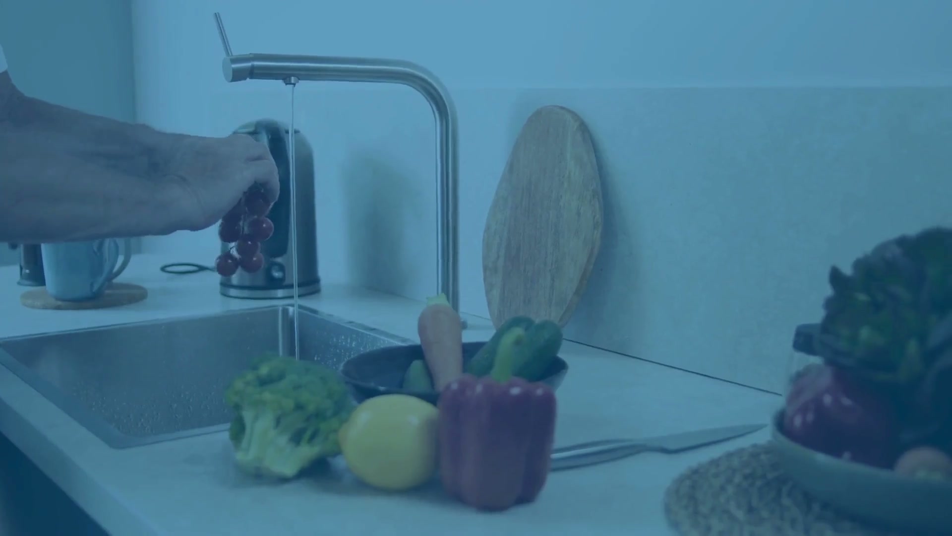 Water running from a kitchen tap while fruit is rinsed at the sink